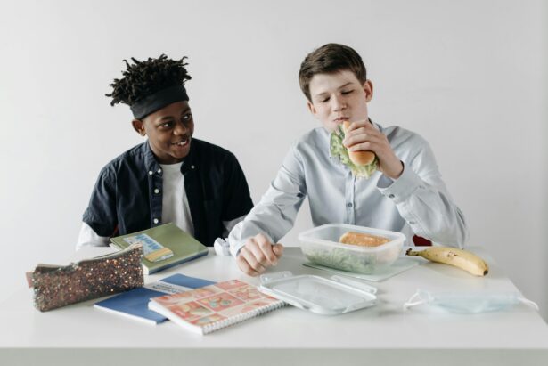 Teen boy eating a sandwich while friend looks on.